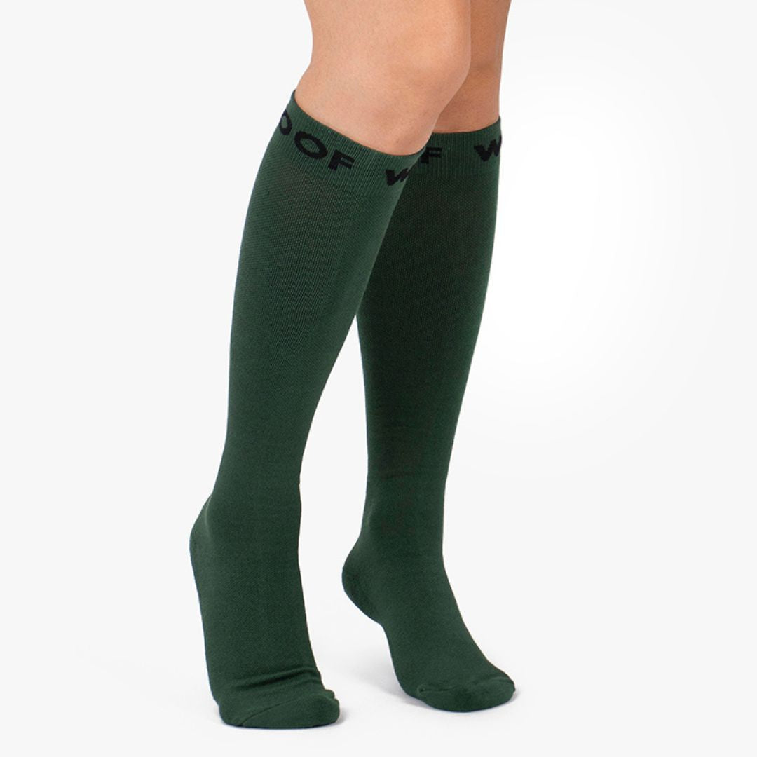 Studio shot of a pair of deep forest green Fern Green Bamboo Compression Socks worn on leg models, featuring a solid tone finish and black "WOOF" woven top cuff branding.   